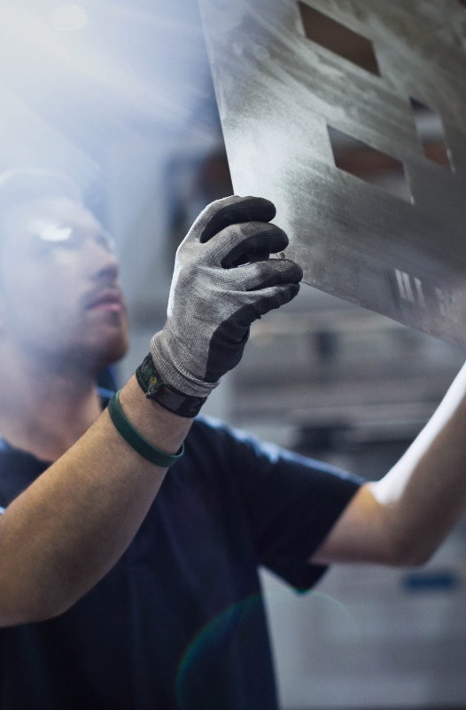 A worker wearing gloves inspects a laser-cut metal sheet under bright industrial lighting.